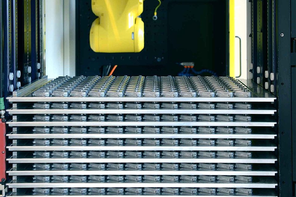 Gelber Industrieroboterarm in schwarzer Maschinenanlage mit Stapeln metallischer Platten.